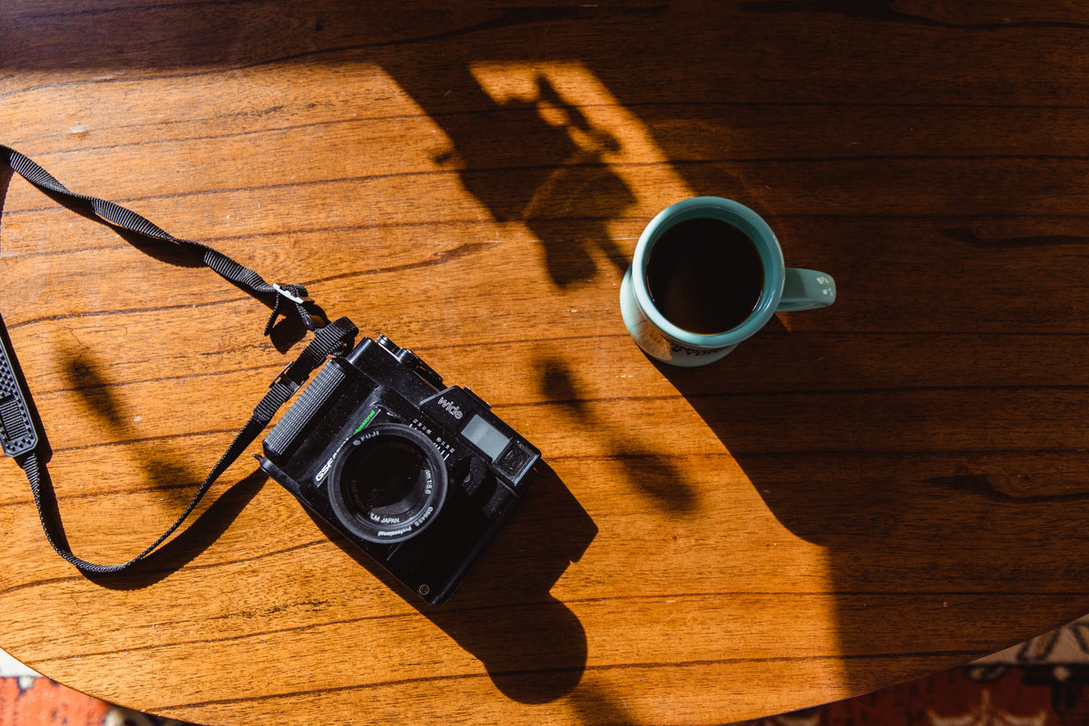 A film camera and a cup of coffee on a wooden table in afternoon light